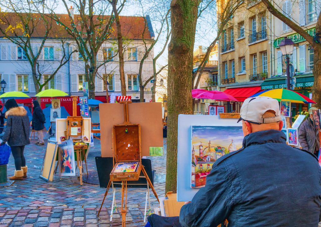 Ulični slikar u Pragu, okružen svojim umetničkim delima, dodaje živopisne boje atmosferi gradskog trga.