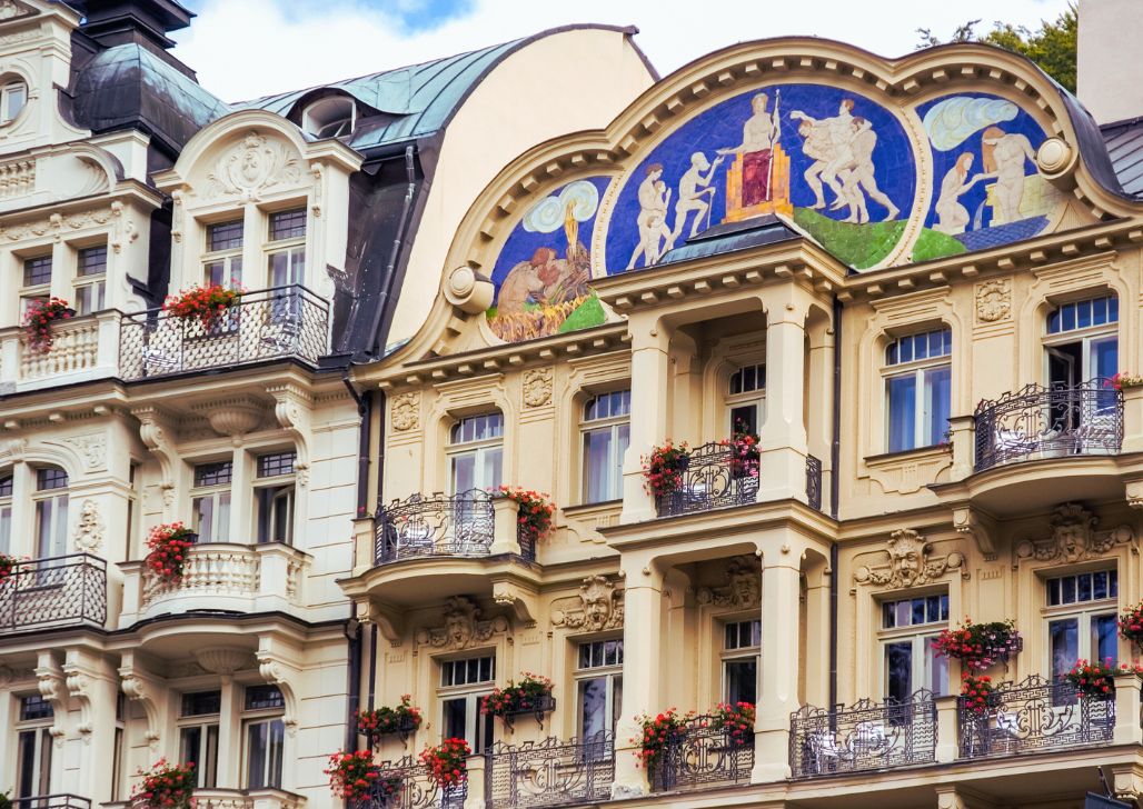 Bogato ukrašena fasada zgrade u Karlovim Varima s muralima, balkonima i cvjetnim aranžmanima.