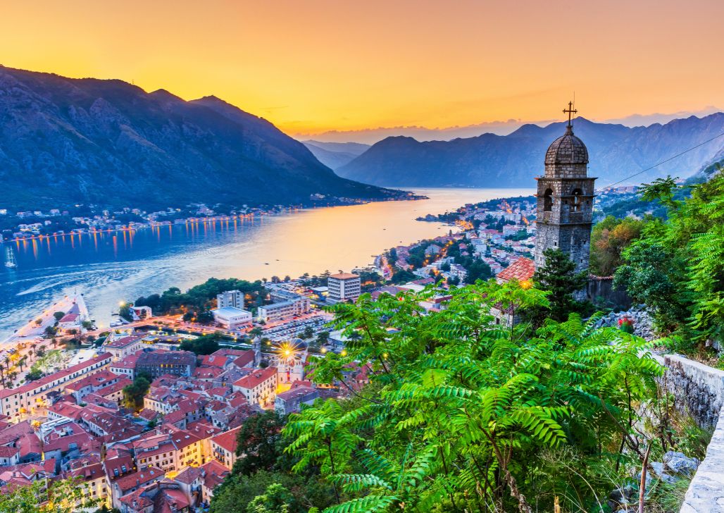 Kotorski zaliv i grad Kotor obasjani narandžastim nebom u zalasku sunca.
