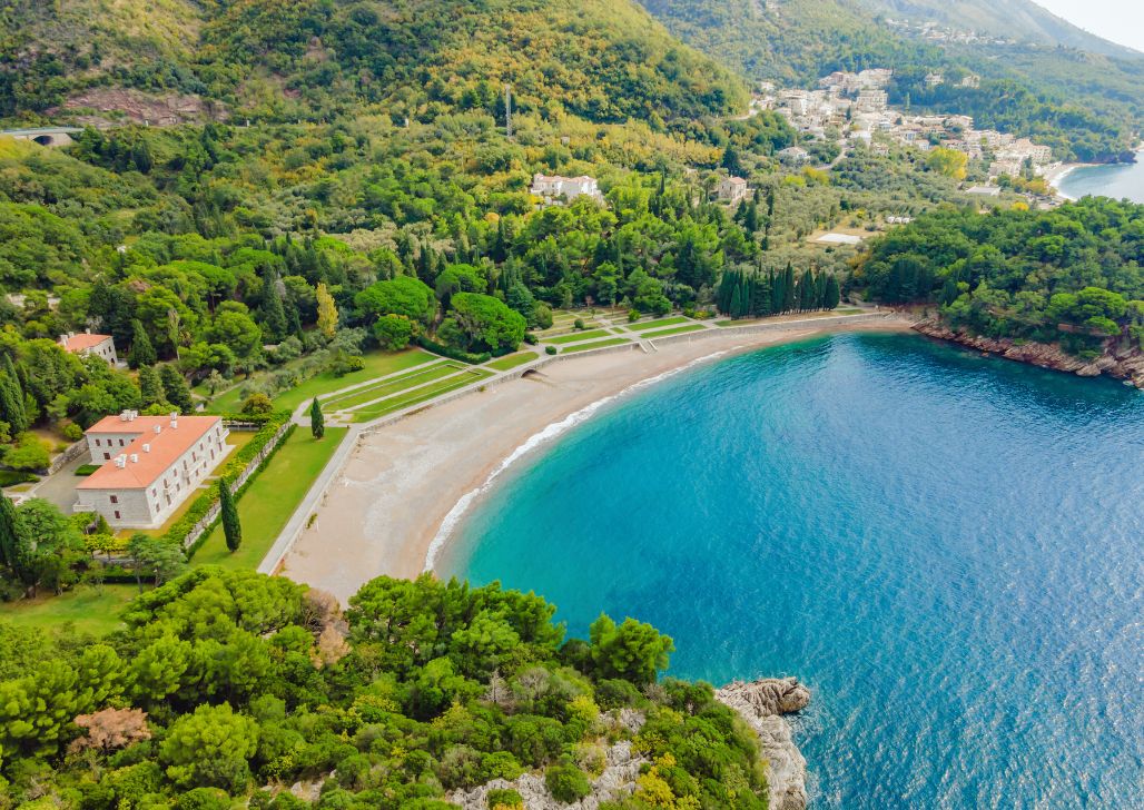 Kraljičina plaža u Crnoj Gori sa bistrom plavom vodom okružena drvećem. 