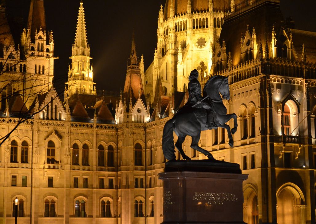 Silueta konjanika pred osvetljenim Mađarskim parlamentom noću.