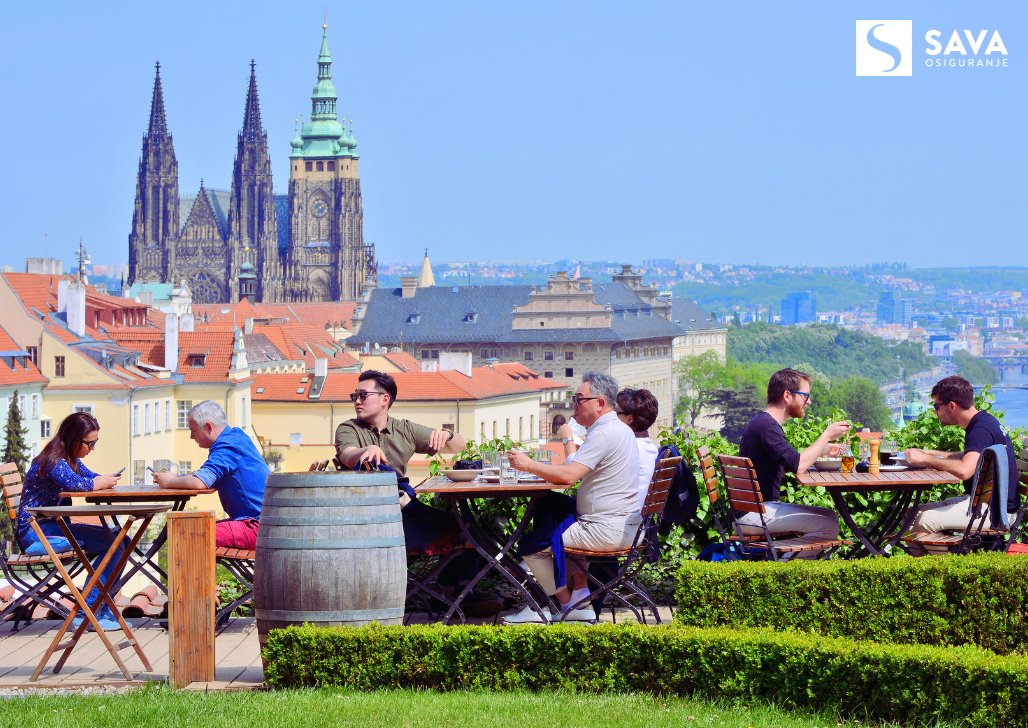 Ljudi uživaju u pivu s pogledom na Praški hrad.