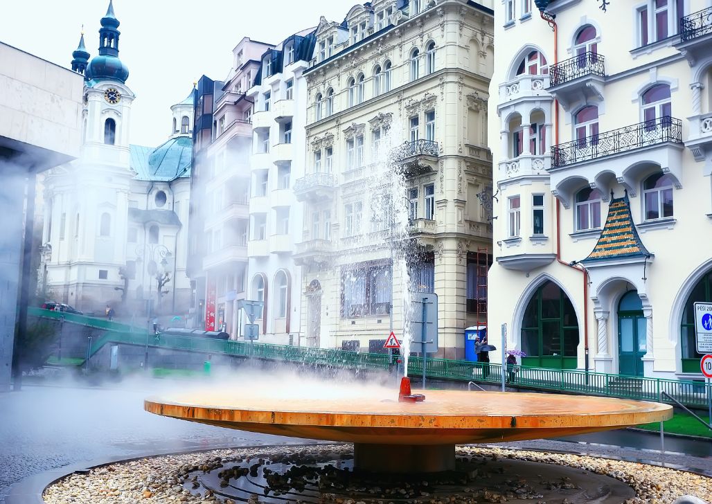 Dimna termalna fontana u centru Karlovih Vari sa historijskim građevinama u pozadini.