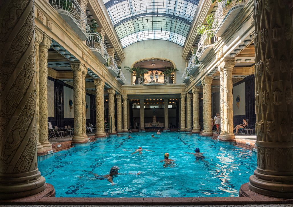 Unutrašnjost Gellért banje, sa plavim bazenom, ljudima koji se kupaju i klasičnom arhitekturom. Najbolje banje u Mađarskoj.