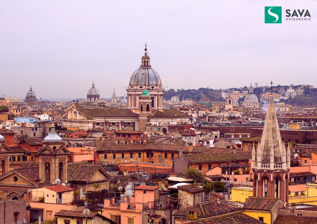 Prostrani pogled na krovove Rima sa istorijskim crkvama i zgradama koje se ističu na horizontu.