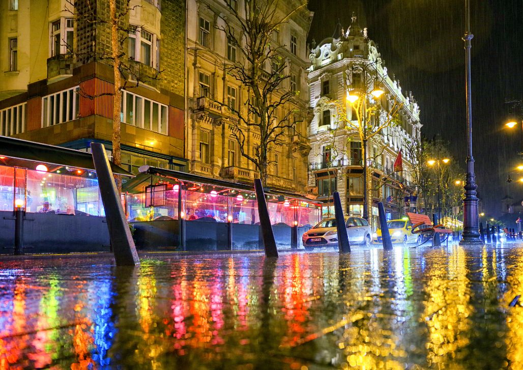 Kišna noć u Budimpešti sa odbljeskom uličnih svetla na mokrom trotoaru.