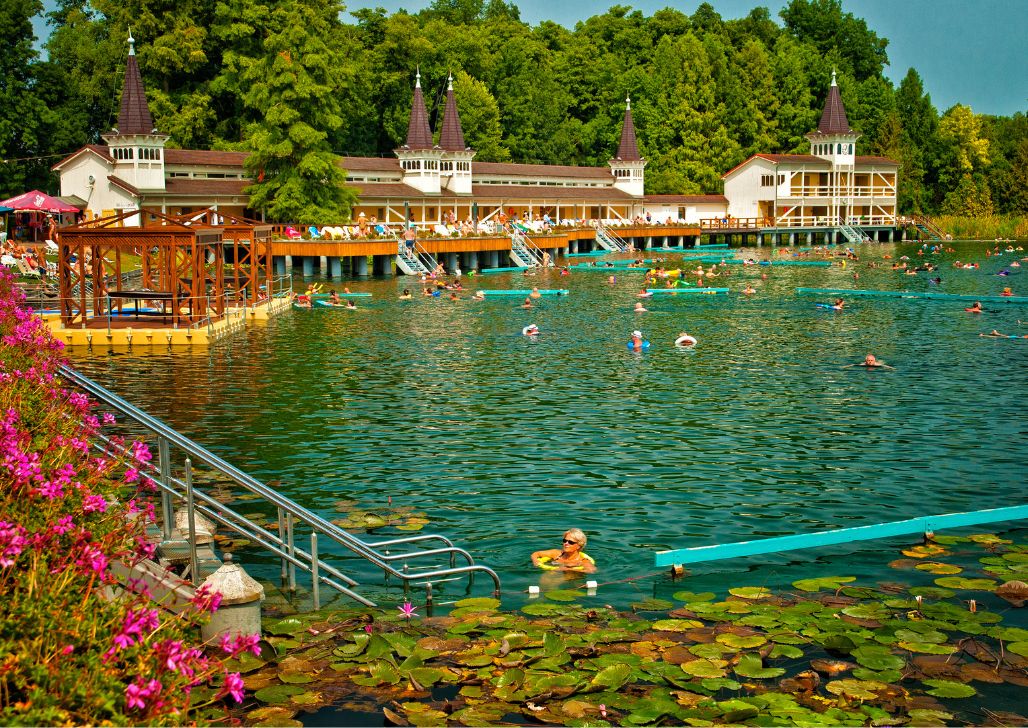 Panoramski pogled na termalno jezero Hévíz, sa ljudima koji se kupaju i plutajućim platformama okruženim zelenilom.